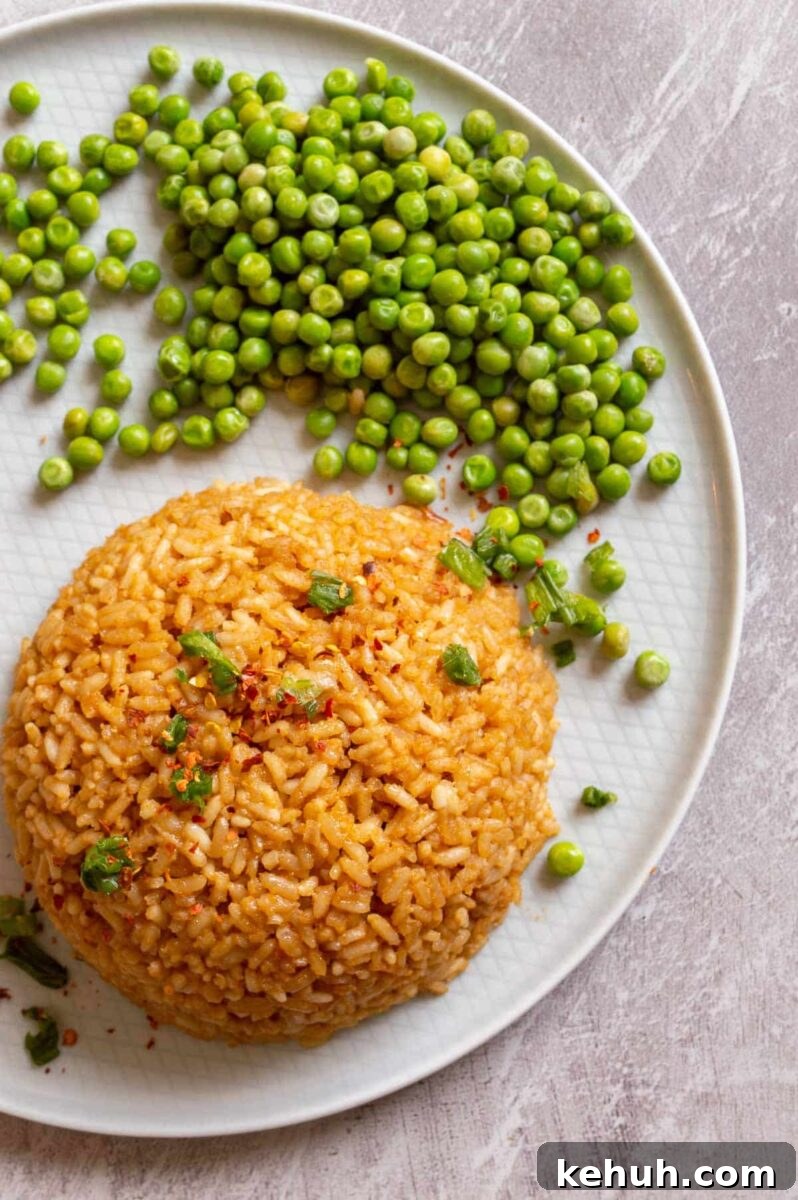 A mound of brown-colored rice on a pale grey plate with green peas.